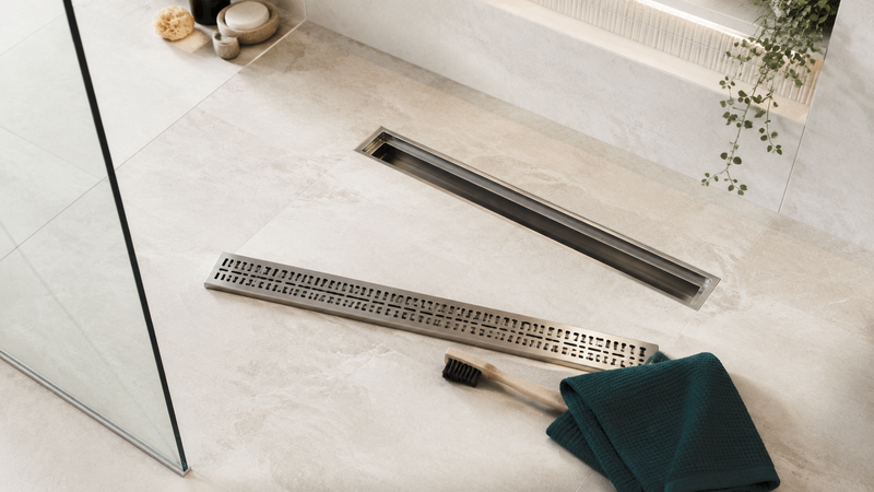 Clean walk-in shower drain with the grate removed and maintenance tools beside it