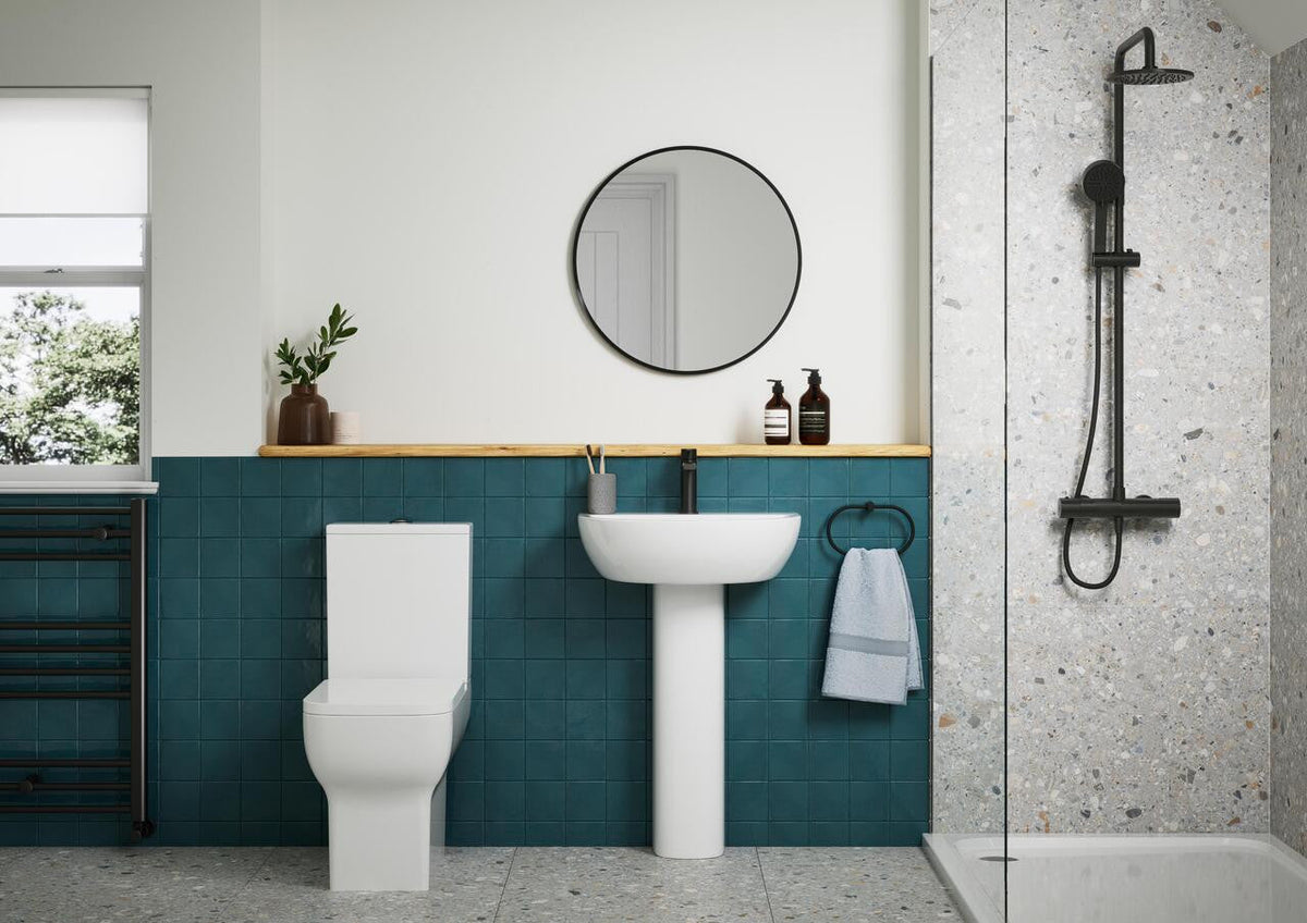 White full pedestal washbasin with black tap in a teal-tiled bathroom